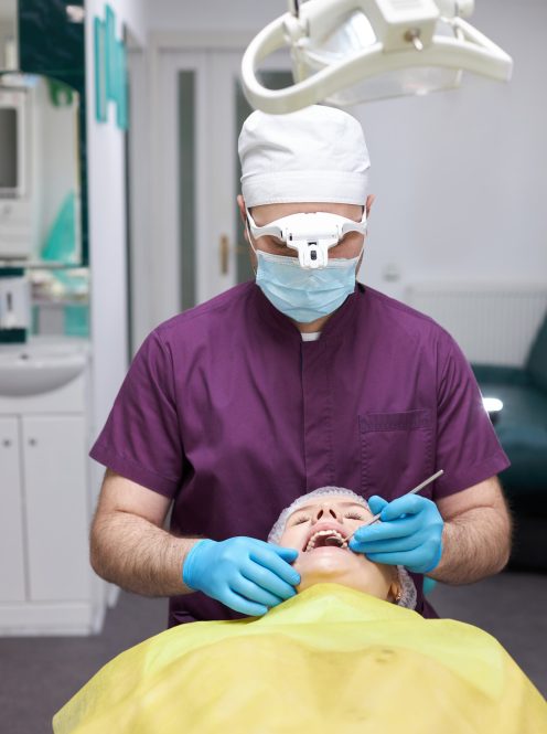Experienced dentist hygienist using dental dental probe, checks woman's teeth in a dentistry clinic